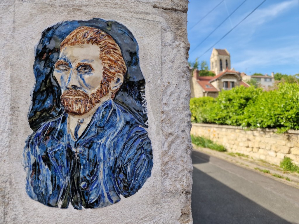 Un portrait de Van Gogh dans une rue d'Auvers-sur-Oise, avec l'église Notre-Dame en arrière-plan.